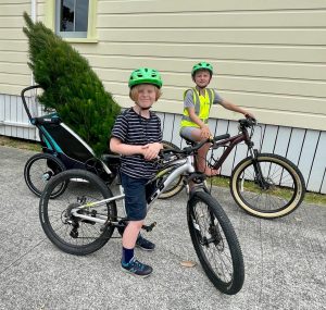 two kids with bikes. In the back of one cargo bike is a christmas tree.