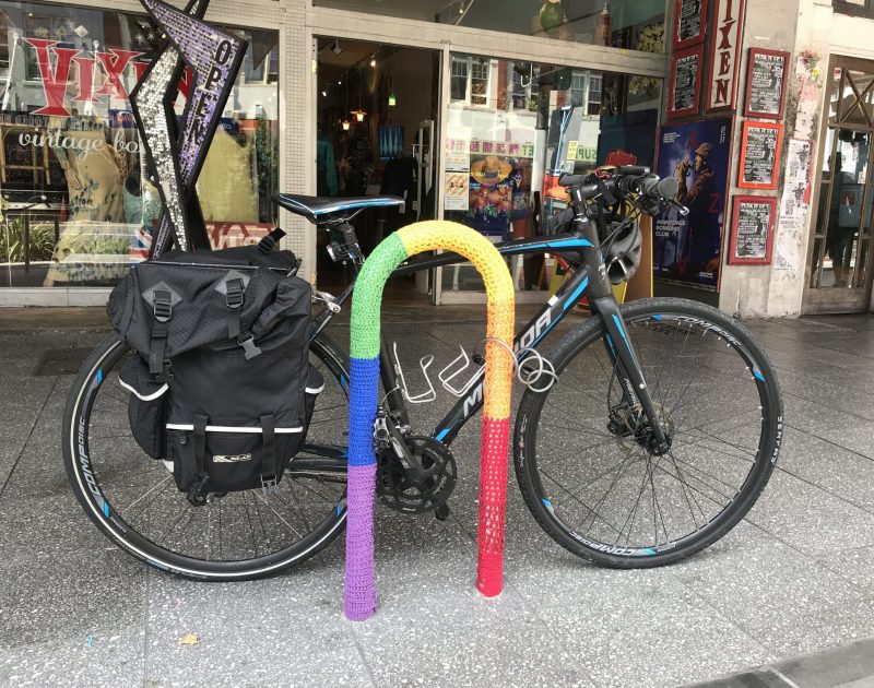 A bike park with a rainbow cover, a bike is locked to it.