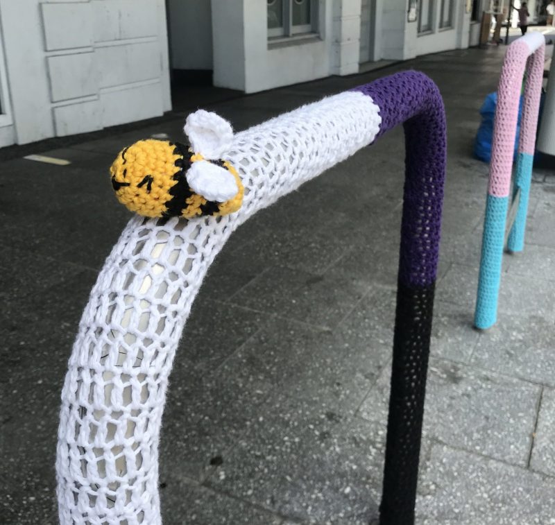 A bee on a bike park decorated with a nonbinary flag. 