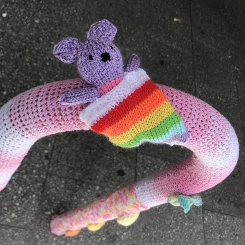 A bear in a rainbow sleeping bag, attached to a bike park.