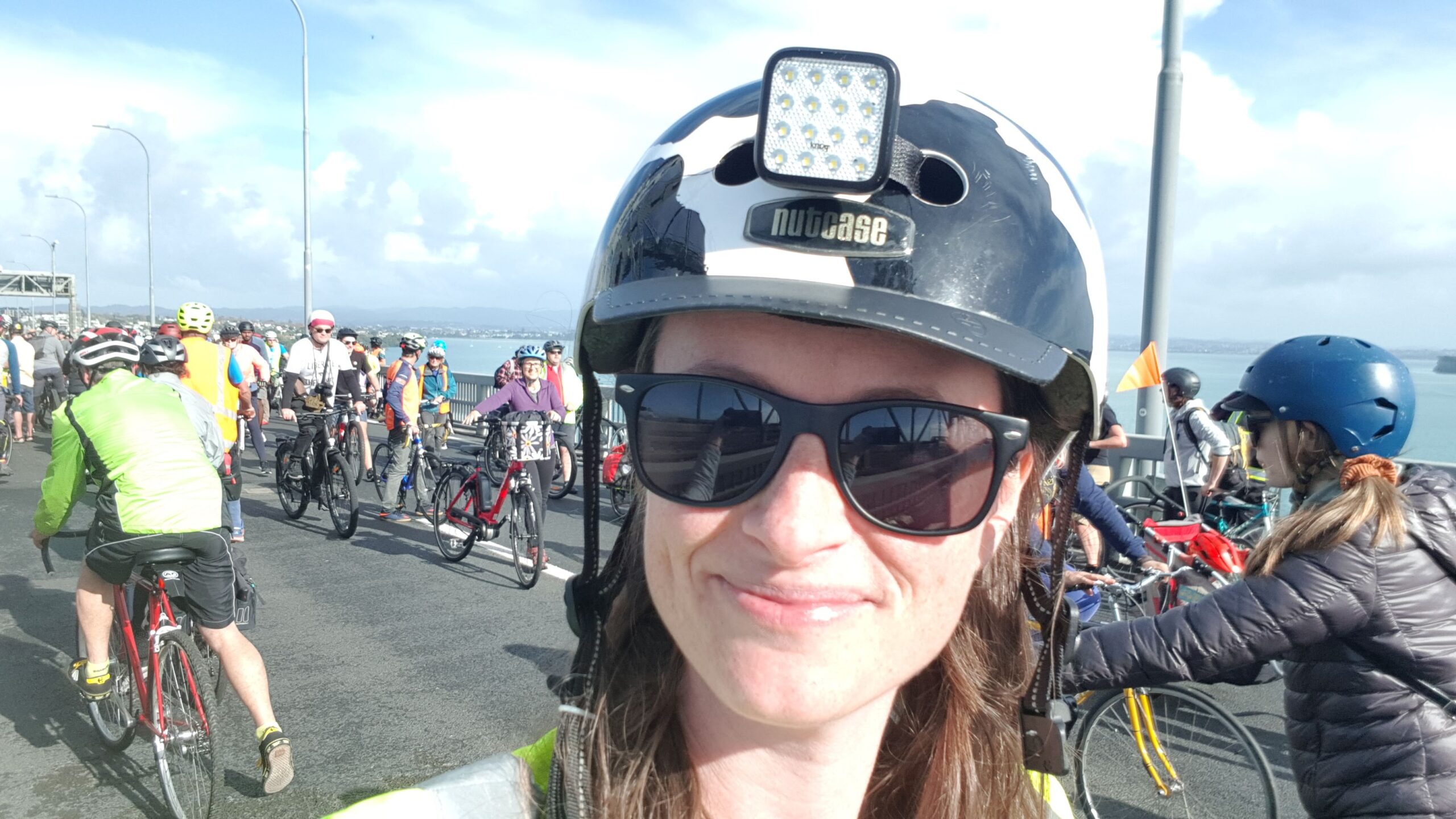 Megan taking a selfie on the Harbour Bridge with her helmet on. In the background the bridge is crowded with people riding bikes as part of a demonstration