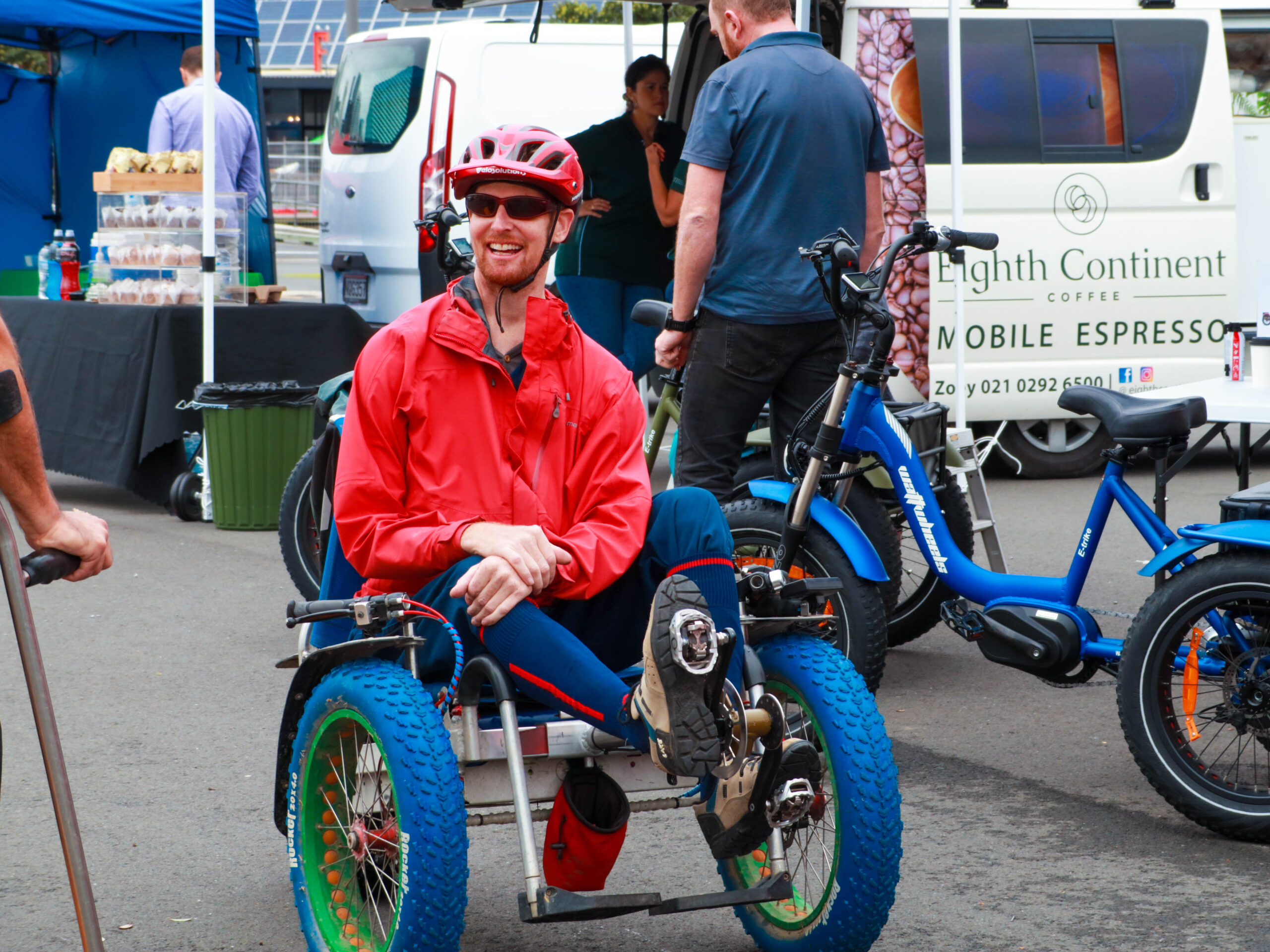 Andrew from MOTOM smiles. He is wearing a helmet and sitting in his powered all-terrain MOTOM chair with his feet on the pedals.