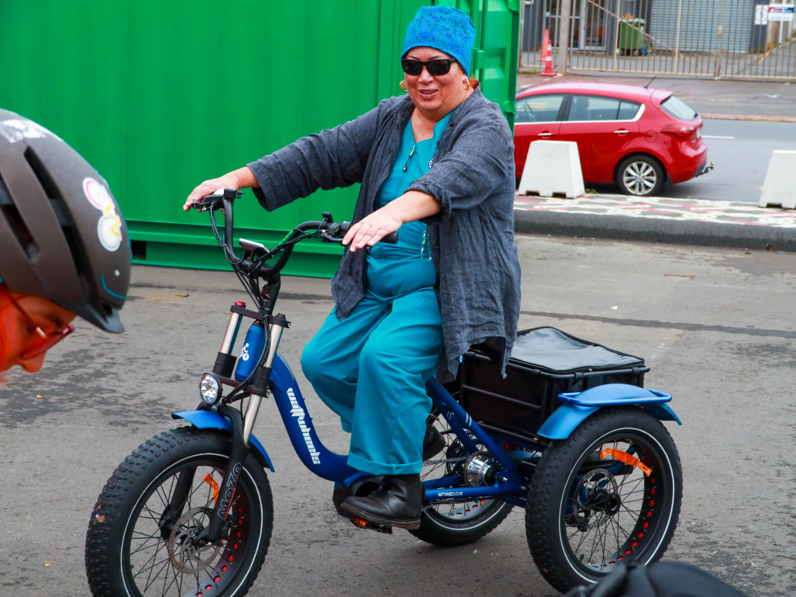 A person smiles. They are sitting on a blue electric tricycle