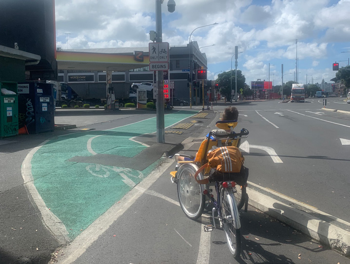 Quay street cycleway and a wheelchair bike with someone sitting in the wheelchair on the front. The two-way cycleway turns sharply from the road onto the footpath. 