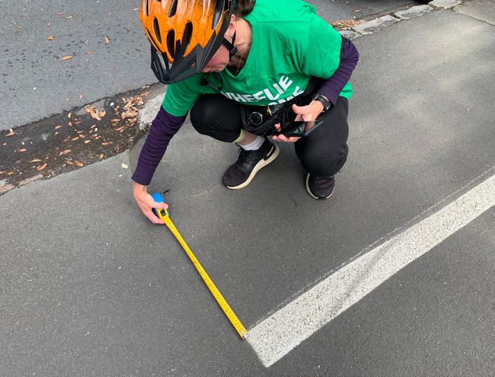 A person uses a tape measure to measure the width of the painted line on the shared pathway on Tāmaki Drive