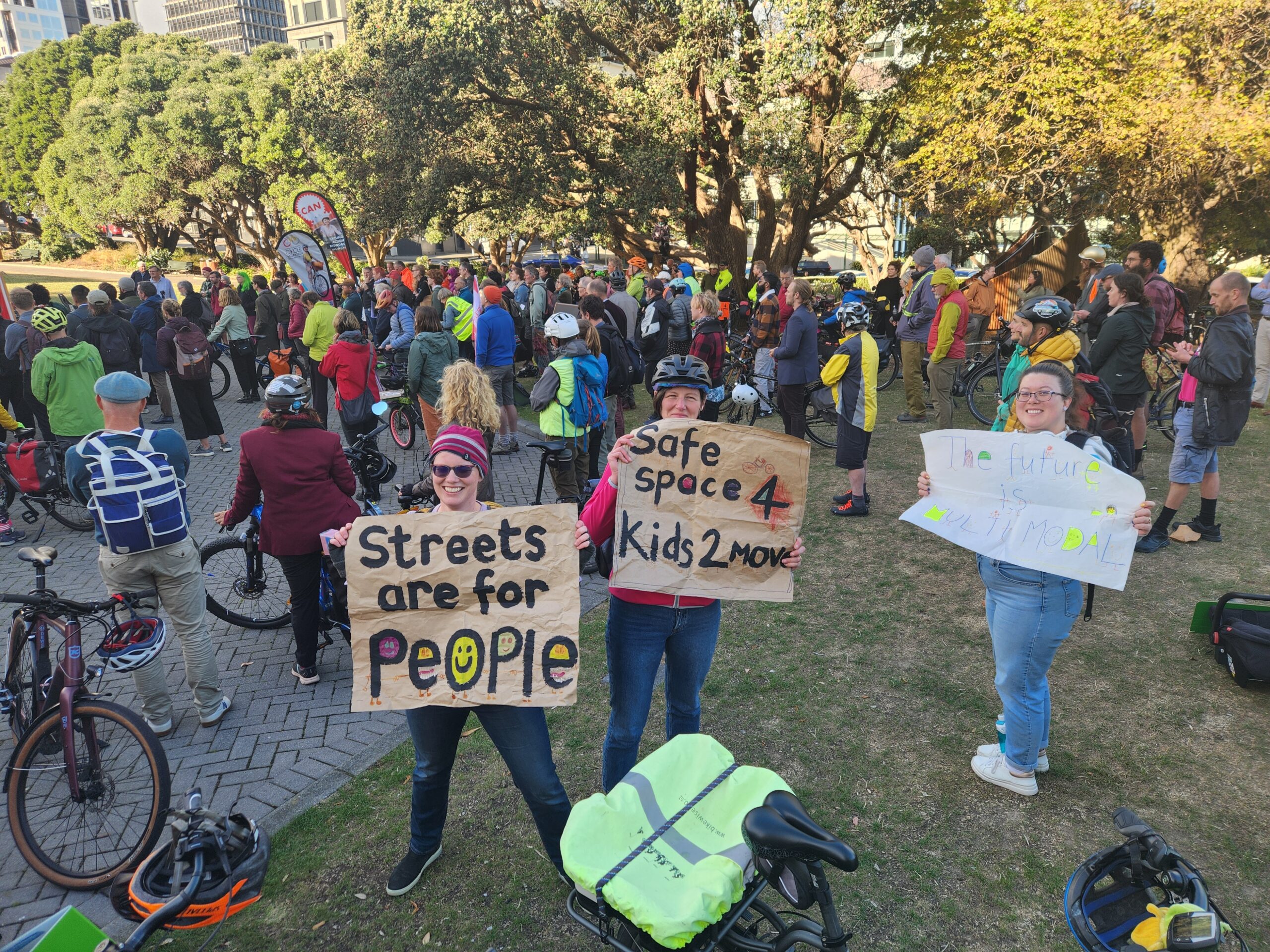 a crowd at the rally, with some people holding signs which say "streets are for people" and "safe space for kids to move". 