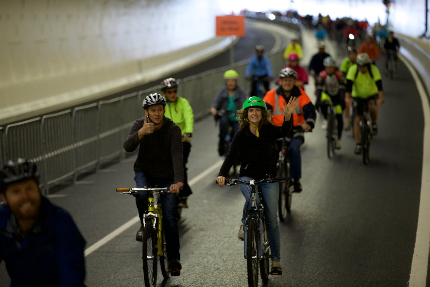 cyclists wave as many cycle through a tunnel
