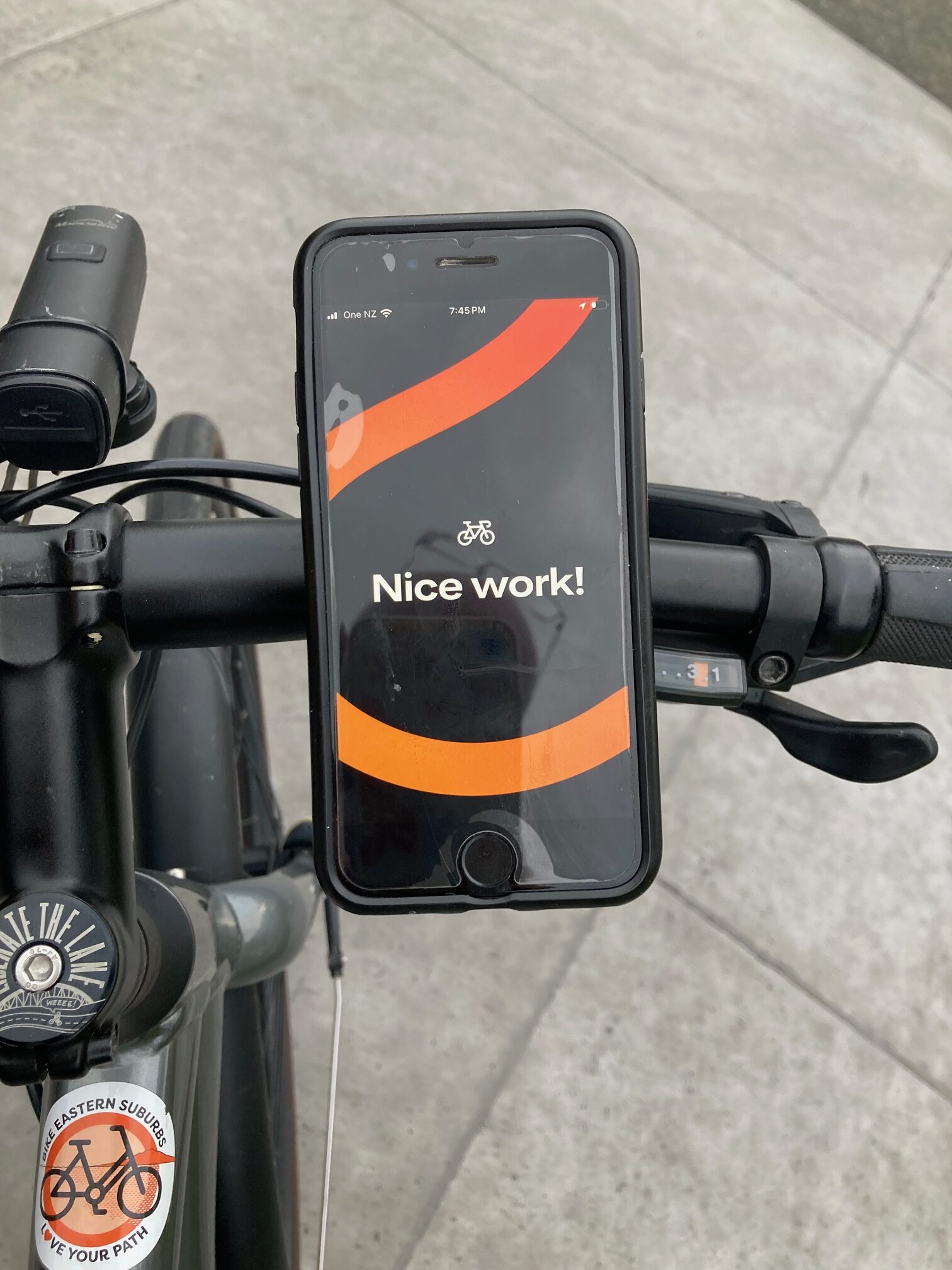 A phone is attached to bike handlebars. The screen says "nice work"