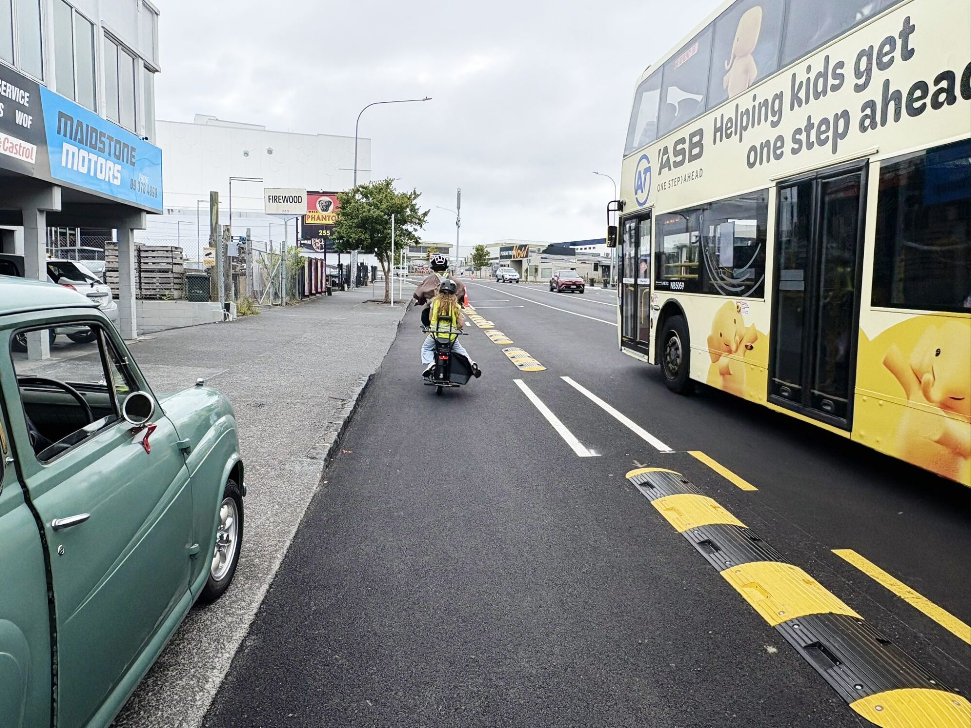 A child rides on the back of a cargo bike in the bike lane while a bus rolls alongside in the vehicle lane