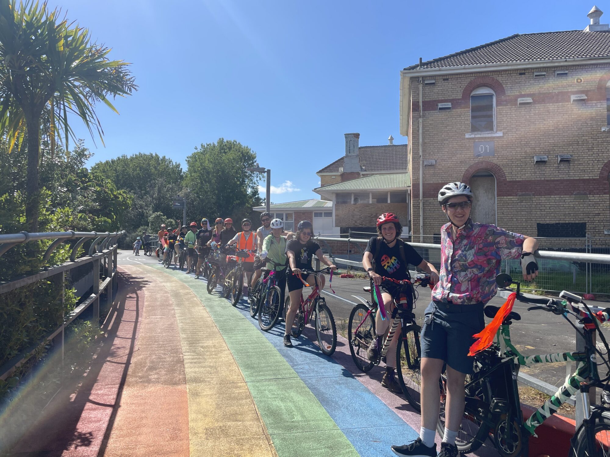 A group of bike riders lean against the fence along the rainbow cycleway