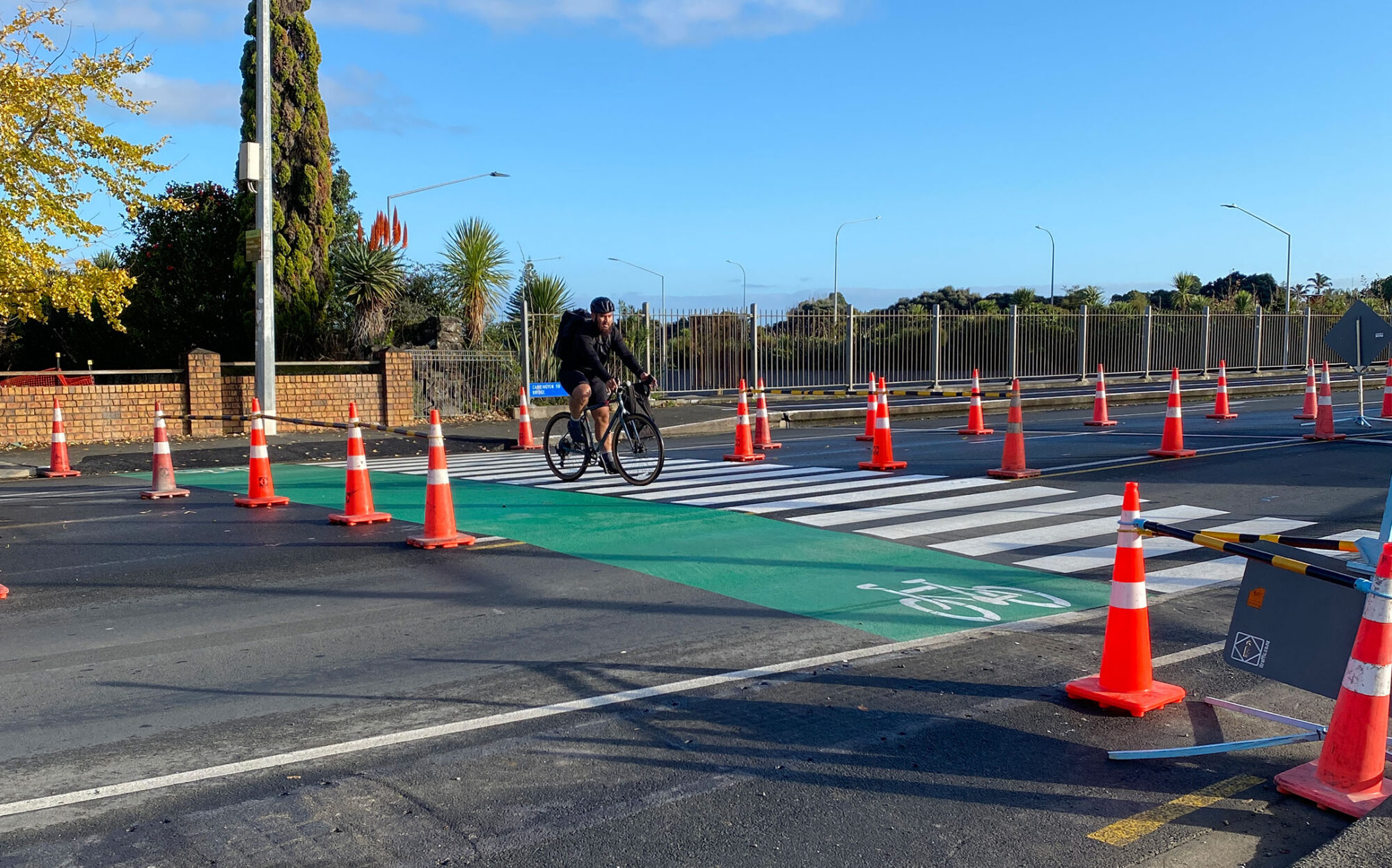 A temporary crossing marked out with orange cones. You can see a green bike side and a striped pedestrian side. A cyclist is in the middle of the crossing.
