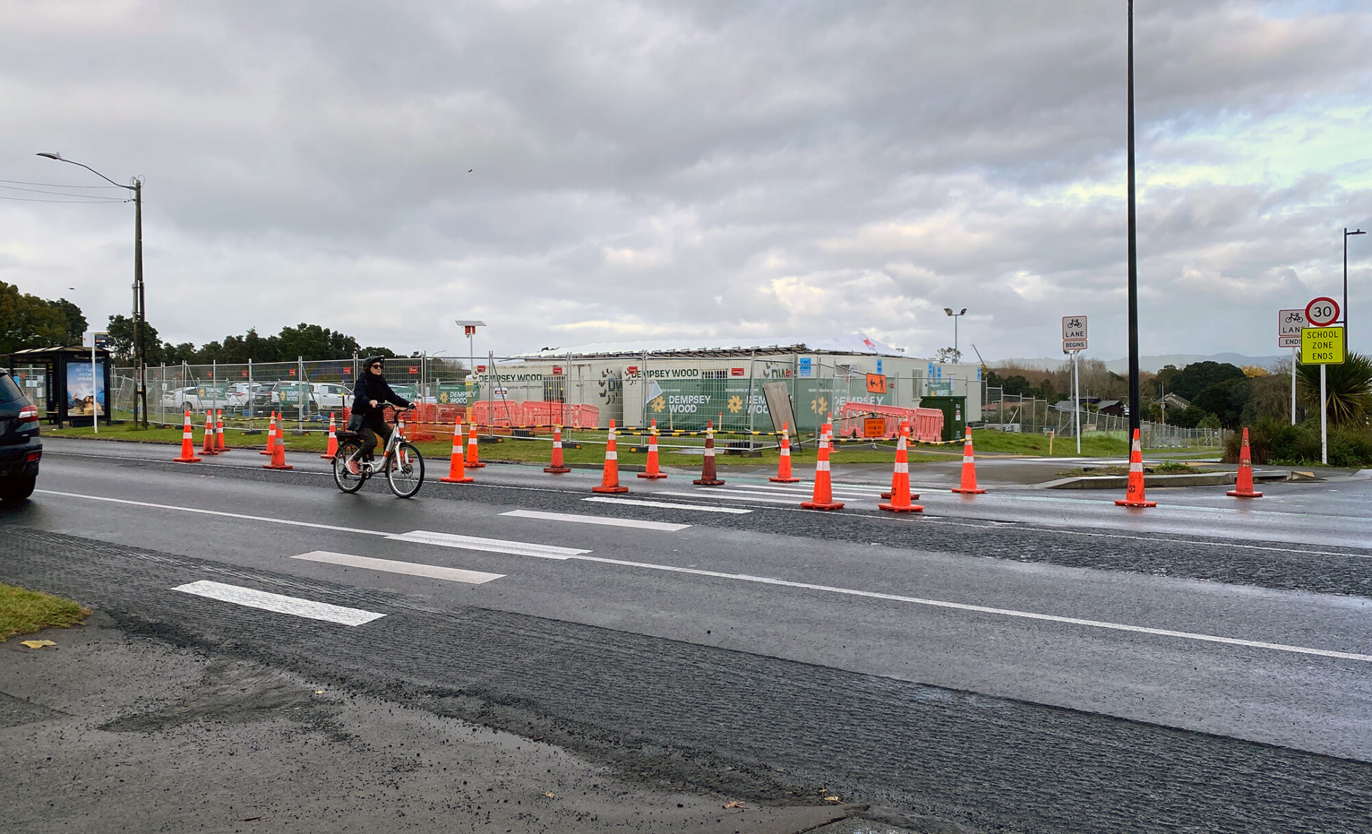 A cyclist takes the lane down a road narrowed by construction cones. There's a temporary zebra crossing in the foreground.